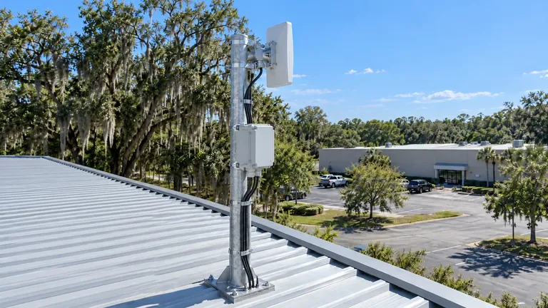 Point-to-point wireless radio on a galvanized mast on a warehouse roof in Ocala, aimed at a second building across the parking lot