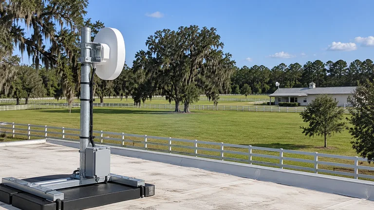 Point-to-point wireless radio on a rooftop mast aimed across a horse-farm pasture toward a second building in Ocala