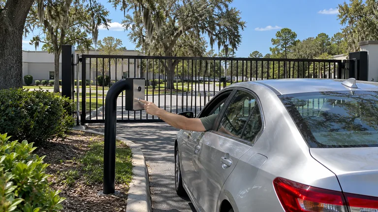 Driver reaching a curbside video intercom pedestal at a controlled commercial vehicle gate