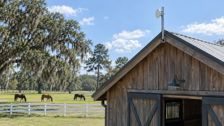 Point-to-point radio on a short mast at a horse barn gable aimed across a pasture with horses and live oaks