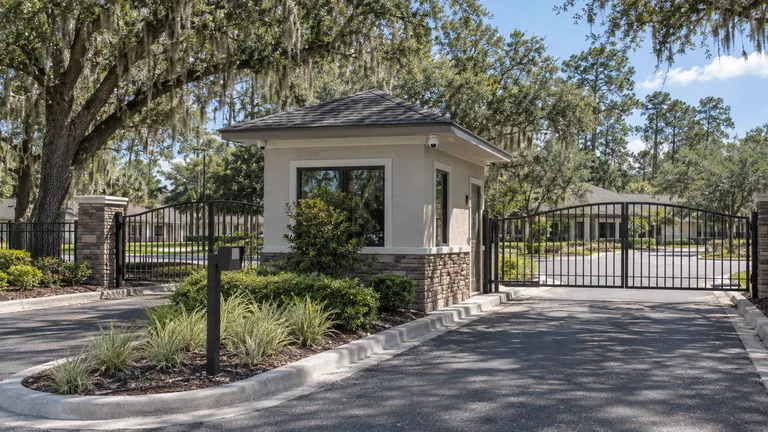 Multifamily community entrance with a gatehouse, vehicle gate, keypad pedestal and dome cameras under the eave