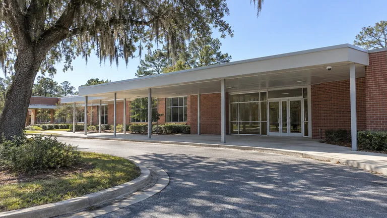 Single-story school entrance with a drop-off loop, covered walkway and a dome camera under the canopy