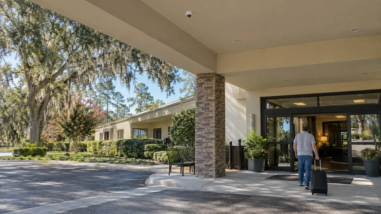 Hotel porte-cochere in Ocala with a guest arriving, glass lobby doors and a dome camera on the canopy ceiling