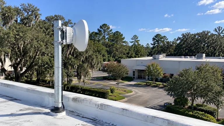 Point-to-point wireless radio on a galvanized mast on a warehouse roof in Ocala, aimed at a second building across the parking lot